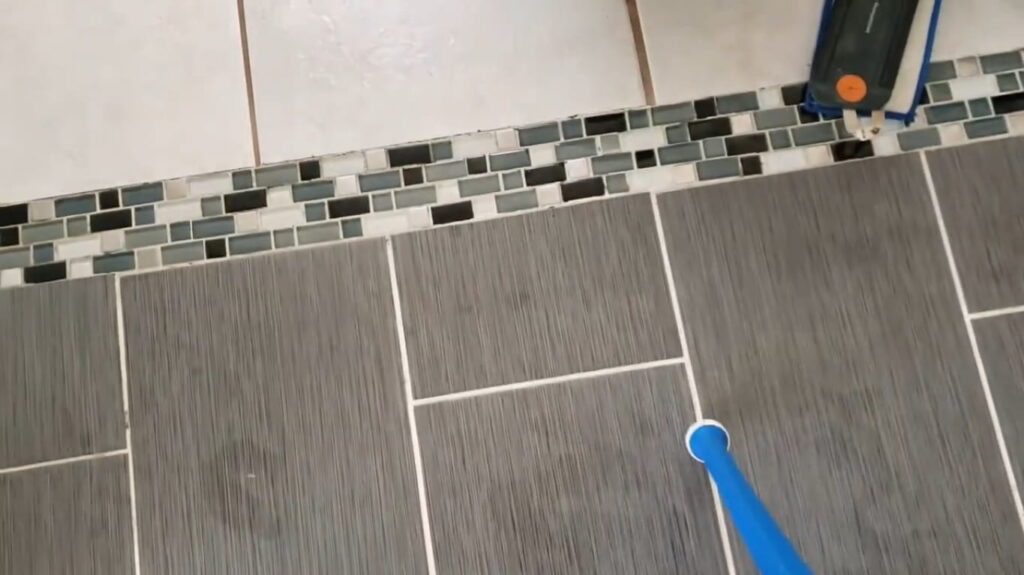 A small brush being used to scrub paint out of the grout lines between ceramic tiles.